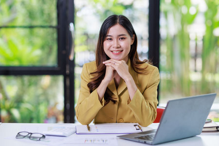 Concept of business office woman working,Businesswoman smile while working about her invesment plan with analyzing document and business investment graph data by using laptop on desk in workstation.の写真素材