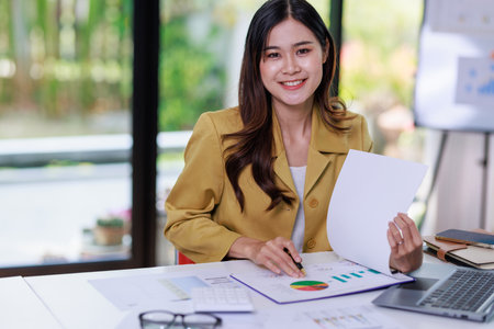 Concept of business office woman working,Businesswoman smile while working about her invesment plan with analyzing document and business investment graph data by using laptop on desk in workstation.の写真素材