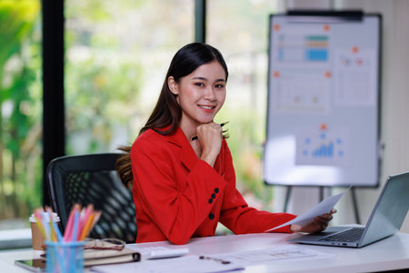 Concept of business office woman working,Businesswoman smile while working about her invesment plan with analyzing document and business investment graph data by using laptop on desk in workstation.の写真素材