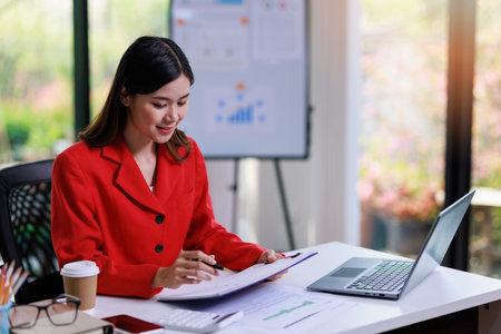 Concept of business office woman working,Businesswoman working about her invesment plan with analyzing document and business investment graph data by using laptop on desk in workstation.の写真素材