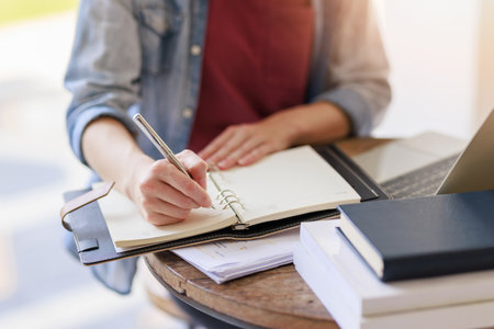 Education concepts, Close up high school young female student or college student sitting and writing on notebook for homework research while wating for class in universityの写真素材