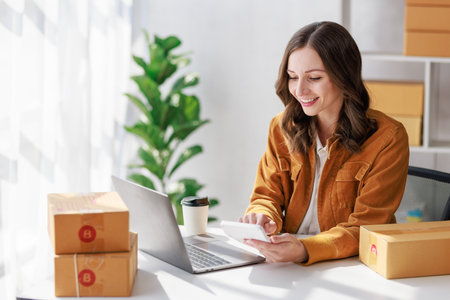 Concept of parcel delivery and selling online, Female seller or retailer using laptop to check sales of the day on online store to be packed into the parcel and ready to deliver to the customerの写真素材