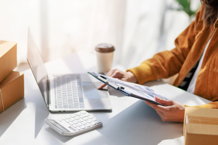 Concept of parcel delivery and selling online, Female seller or retailer using laptop to check sales of the day on online store to be packed into the parcel and ready to deliver to the customerの写真素材
