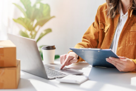 Concept of parcel delivery and selling online, Female seller or retailer using laptop to check sales of the day on online store to be packed into the parcel and ready to deliver to the customerの写真素材