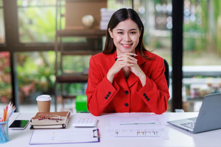 Concept of business office woman working,Businesswoman smile while working about her invesment plan with analyzing document and business investment graph data by using laptop on desk in workstation.の写真素材