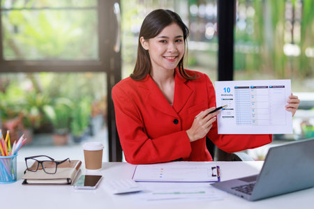 Concept of business office woman working,Businesswoman smile while working about her invesment plan with analyzing document and business investment graph data by using laptop on desk in workstation.の写真素材