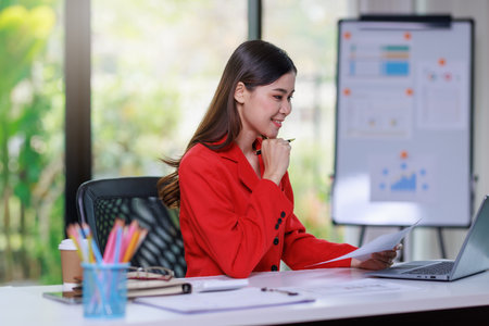 Concept of business office woman working,Businesswoman smile while working about her invesment plan with analyzing document and business investment graph data by using laptop on desk in workstation.の写真素材