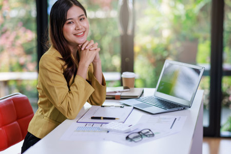 Concept of business office woman working,Businesswoman smile while working about her invesment plan with analyzing document and business investment graph data by using laptop on desk in workstation.の写真素材