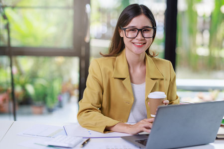 Concept of business office woman working,Businesswoman smile while working about her invesment plan with analyzing document and business investment graph data and holding coffee cup in workstationの写真素材
