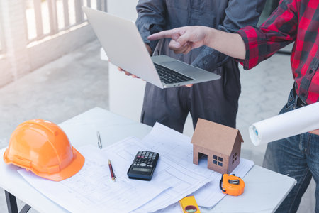 Construction concept of Engineer and Architect working at Construction Site with blue print, Engineer and Architect discussing construction plan with computer laptop calculatorの写真素材
