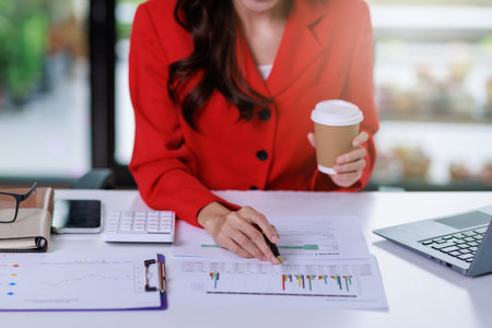Concept of business office woman working,Close up businesswoman checking her invesment plan with analyzing document and business investment graph data by using computer laptop while holding coffee cupの写真素材