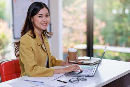 Concept of business office woman working,Businesswoman smile while working about her invesment plan with analyzing document and business investment graph data by using laptop on desk in workstation.の写真素材