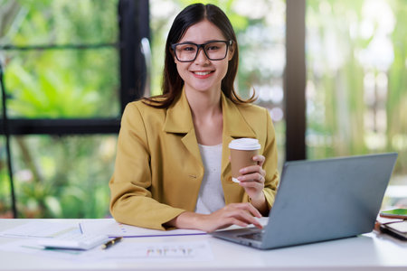 Concept of business office woman working,Businesswoman smile while working about her invesment plan with analyzing document and business investment graph data by using laptop on desk in workstation.の写真素材