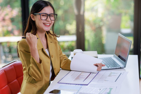 Concept of business office woman working,Businesswoman smile while working about her invesment plan with analyzing document and business investment graph data by using laptop on desk in workstation.の写真素材