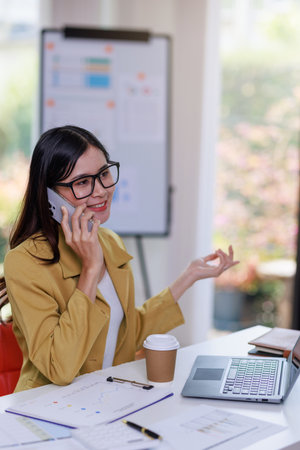 Concept of business office woman working,Businesswoman using smartphone talking to her client about invesment plan and checking  analyzing document and business investment graph data in workstation.の写真素材