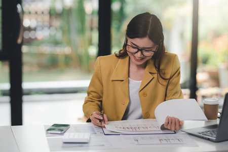 Concept of business office woman working,Businesswoman smile while working about her invesment plan with analyzing document and business investment graph data by using laptop on desk in workstation.の写真素材
