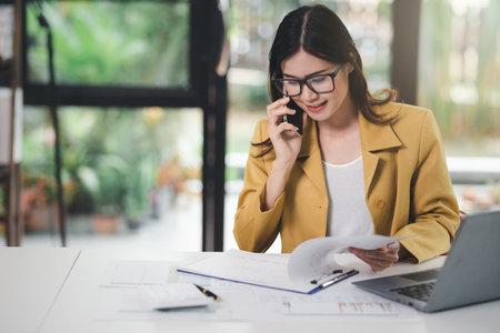Concept of business office woman working,Businesswoman using smartphone talking to her client about invesment plan and checking  analyzing document and business investment graph data in workstation.の写真素材