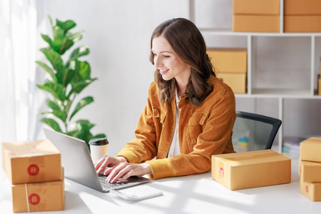 Concept of parcel delivery and selling online, Female seller or retailer using laptop to check sales of the day on online store to be packed into the parcel and ready to deliver to the customerの写真素材