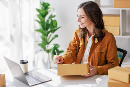 Concept of parcel delivery and selling online, Female seller or retailer using laptop to check sales of the day on online store to be packed into the parcel and ready to deliver to the customerの写真素材