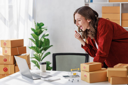 Concept of parcel delivery and selling online, Female seller or retailer using laptop to check sales of the day on online store to be packed into the parcel and ready to deliver to the customerの写真素材