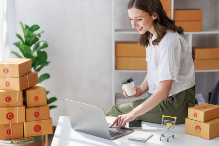 Concept of parcel delivery and selling online, Female seller or retailer using laptop to check sales of the day on online store to be packed into the parcel and ready to deliver to the customerの写真素材