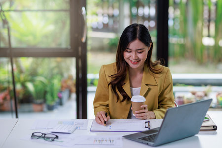 Concept of business office woman working,Businesswoman smile while working about her invesment plan with analyzing document and business investment graph data by using laptop on desk in workstation.の写真素材