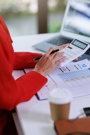 Concept of business office woman working,Businesswoman smile while working about her invesment plan with analyzing document and business investment graph data by using laptop on desk in workstation.の写真素材