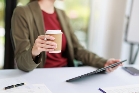 Concept of business office woman working,Closeup businesswoman checking her invesment plan with analyzing document and business investment graph by using calculator and laptop while holding coffee cupの写真素材