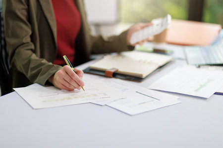 Concept of business office woman working,Businesswoman smile while working about her invesment plan with analyzing document and business investment graph data by using laptop on desk in workstation.の写真素材