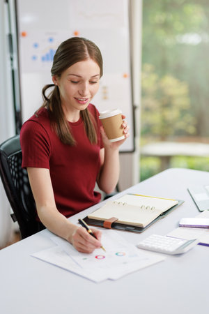 Concept of business office woman working,Businesswoman smile while working about her invesment plan with analyzing document and business investment graph data by using laptop on desk in workstation.の写真素材
