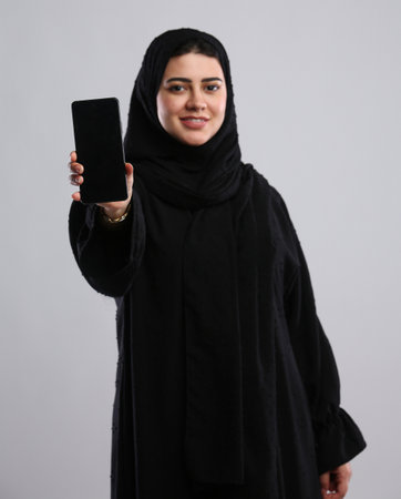 Portrait of a young muslim woman showing mobile phone on grey backgroundの写真素材