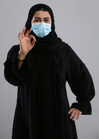 Young muslim woman wearing medical mask and showing ok sign on grey backgroundの写真素材