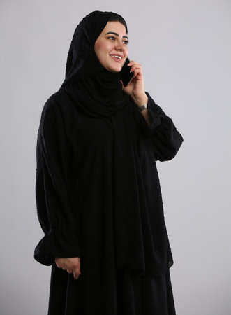 Young muslim woman in black hijab talking on the phone on grey backgroundの写真素材