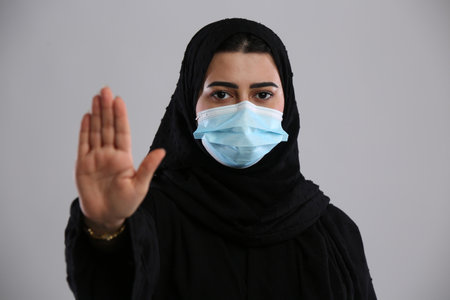 Arabic woman in medical mask showing stop gesture on grey background.の写真素材
