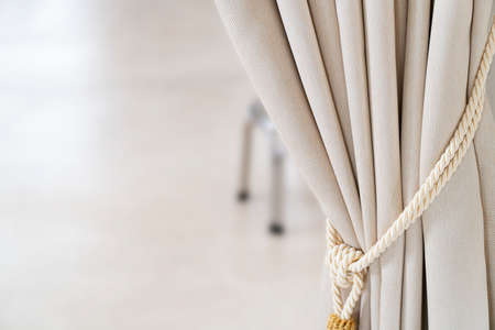 Close-up drapery beige curtain tied with a weave rope.