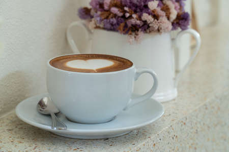 coffee with heart shaped milk froth near window with a vase with dried flower.の写真素材