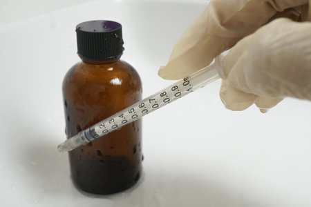 Gloved hand holds syringe next to brown glass bottle, suggesting medical or laboratory setting....