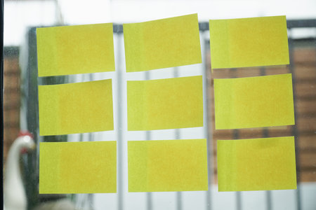 Yellow sticky notes are neatly arranged on glass surface, creating organized and creative display....