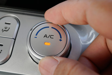 A person adjusting the air conditioning control in a vehicle, with a focus on the dial and indicator light.の写真素材