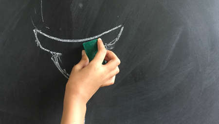 Child hand erasing drawing on blackboard as Stock Image as JPG File