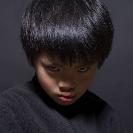 Angry chinese boy portrait on dark background.の写真素材