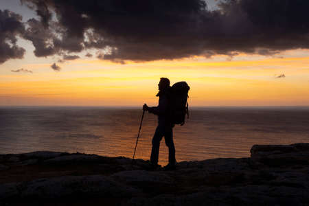 Man with backpack walking alone near the sea at sunset