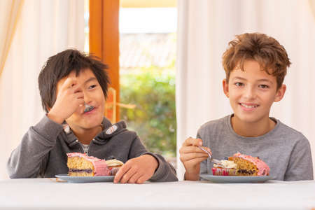 chinese and caucasian children eating cake inside a house, celebrating and having funの写真素材