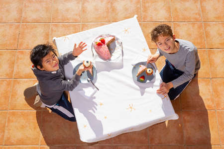 Chinese and caucasian children eating cake on white table. Top view.の写真素材