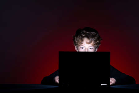 Boy with computer surfing internet alone on dark backgroundの写真素材