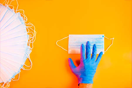 Hand with blue glove holding protective mask on orange background. Selective focus