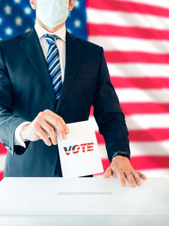 Man dressed in a suit and protective mask voting in the elections for president with the US flag behind him, Selective focusの写真素材