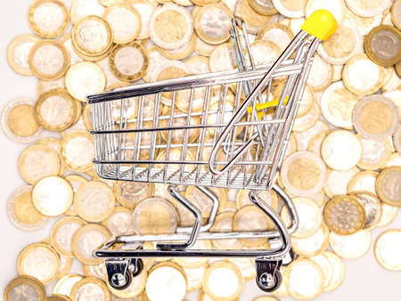 Shopping cart on a lot of coins. Selective focus.