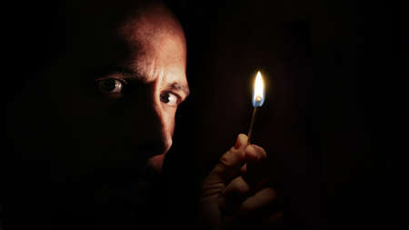 Worried man looking at the camera with a match in the dark. Blackout concept.の写真素材