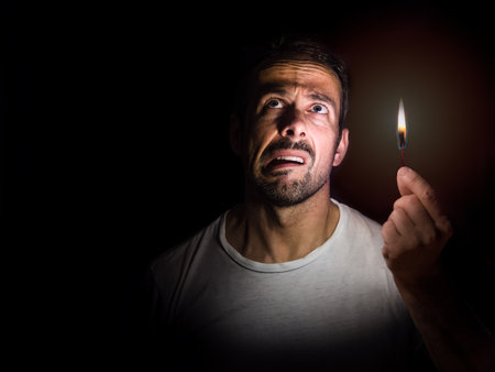 Worried man with a match in the dark. Blackout concept.の写真素材